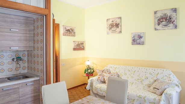 A cozy room with a kitchenette, a floral-patterned sofa, a small table, and wall art. - Eveten 1 - apartment for 4, in town centre, 500 metres from the beach, with parking (Diano Marina)