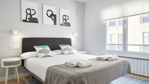 A hotel room with a bed, bedside tables, a window with a view, and artwork on the wall.
