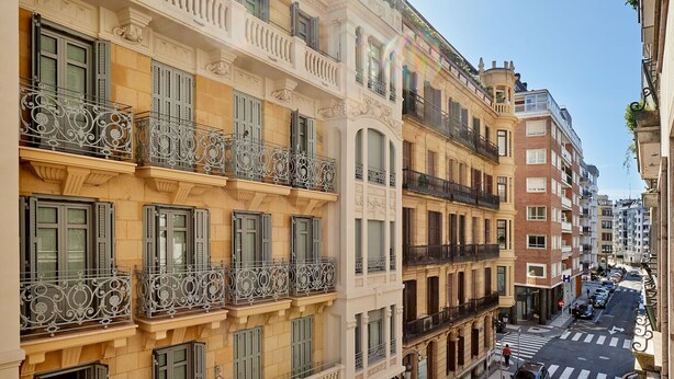 A multi-story building with balconies, a street view, and a clear sky.