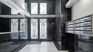 A modern lobby with a black marble floor, a double door with decorative metalwork, and a wall-mounted safe with multiple locks.