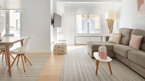 A modern living room with a sofa, a dining table with chairs, and a TV mounted on the wall.