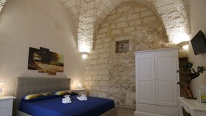 Een slaapkamer met een stenen muur, een bed met blauw beddengoed, een nachtkastje, een kast en een televisie aan de muur.