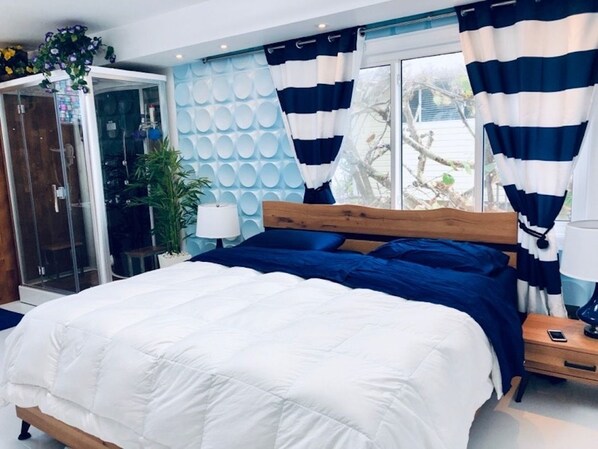 A bedroom with a wooden bed, white and blue bedding, a glass door leading outside, and a view of the outdoors.