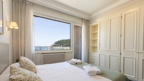A hotel room with a large bed, a view of the sea, and a wardrobe.