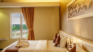 A hotel room with a bed, a window with curtains, a view of greenery, and a decorative wall panel. - Red Chilies Hotel (Surakarta)