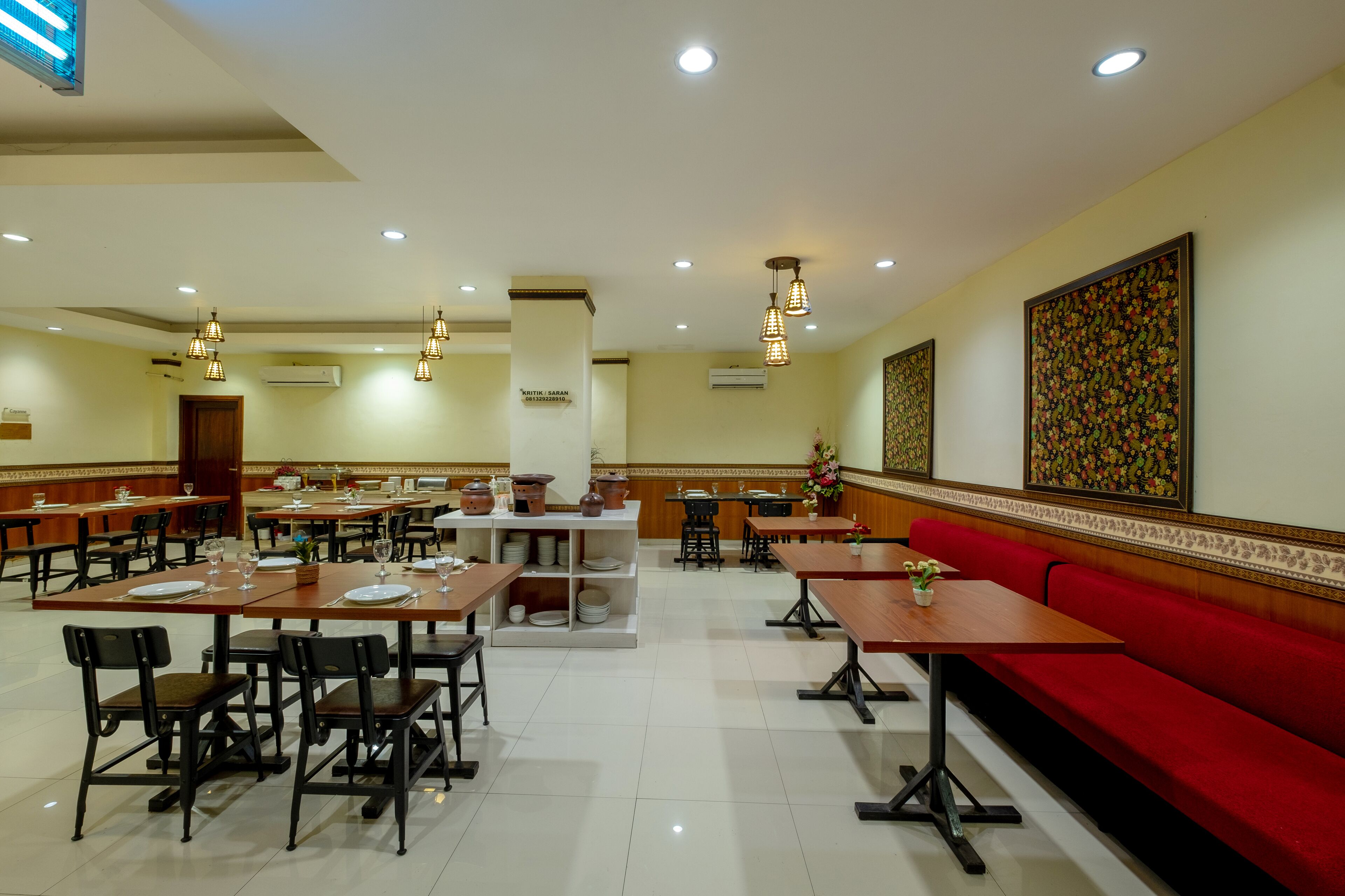 A spacious restaurant with multiple dining tables and chairs, a red cushioned bench, and decorative wall art.