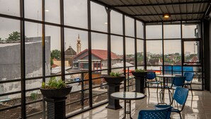 A spacious balcony with large windows, potted plants, and blue chairs. - Red Chilies Hotel (Surakarta)