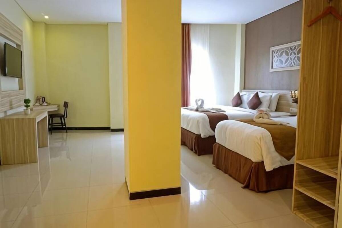 A hotel room with two beds, a desk, and a mirror.