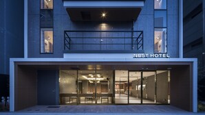 L’entrée d’un hôtel moderne, avec une façade en verre, un comptoir d’accueil bien visible et un balcon.