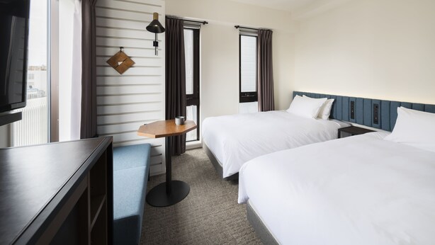 Une chambre d’hôtel avec deux lits, un bureau, une chaise, une télévision et une fenêtre avec des rideaux.