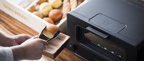 A person using a bread slicer next to a box of assorted bread.