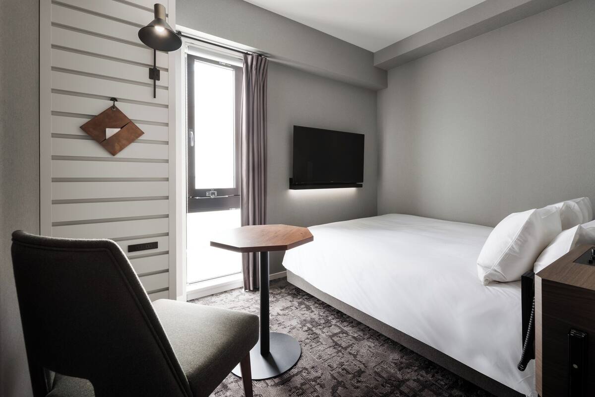 Ein Hotelzimmer mit Bett, Schreibtisch, Stuhl, Fernseher und einem Fenster mit Vorhängen.