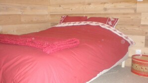 Una cama con colcha y almohadas rojas, un cabecero de madera y un pequeño adorno en el suelo.