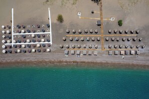 Vue aérienne d’un hôtel situé en bord de mer, avec des rangées de parasols de plage, des chaises longues et une mer turquoise d’une clarté saisissante.