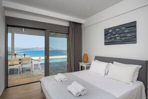 A hotel room with a bed, a painting, a nightstand, and a view of the sea.