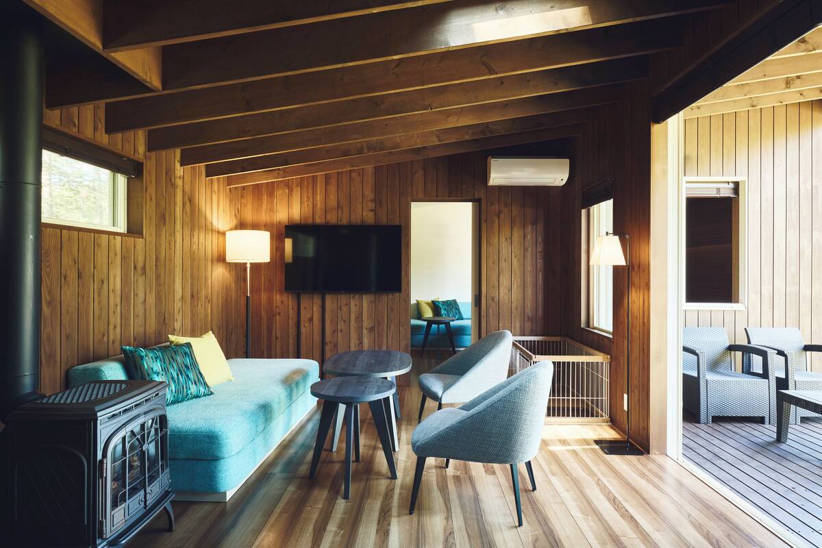 Interior acogedor de una cabaña con detalles de madera, una chimenea, un sofá, un televisor y un balcón con mobiliario exterior.