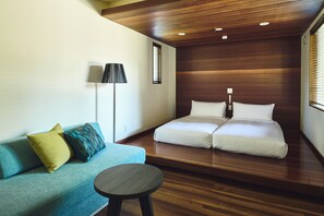 Una habitación con techo de madera, un sofá con cojines, una mesita redonda y una cama con almohadas.