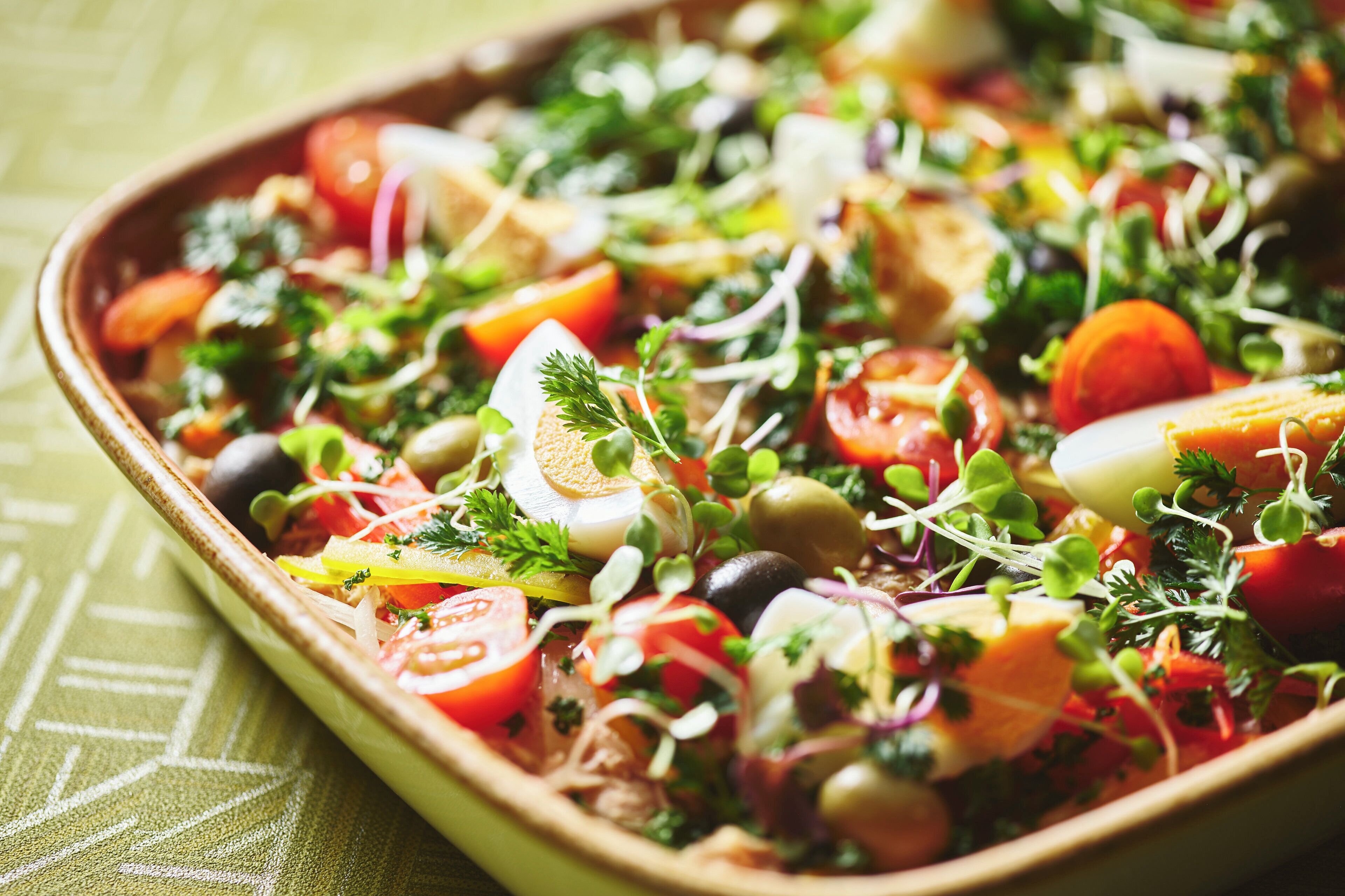 A rectangular dish with a variety of vegetables, herbs, and possibly some protein.