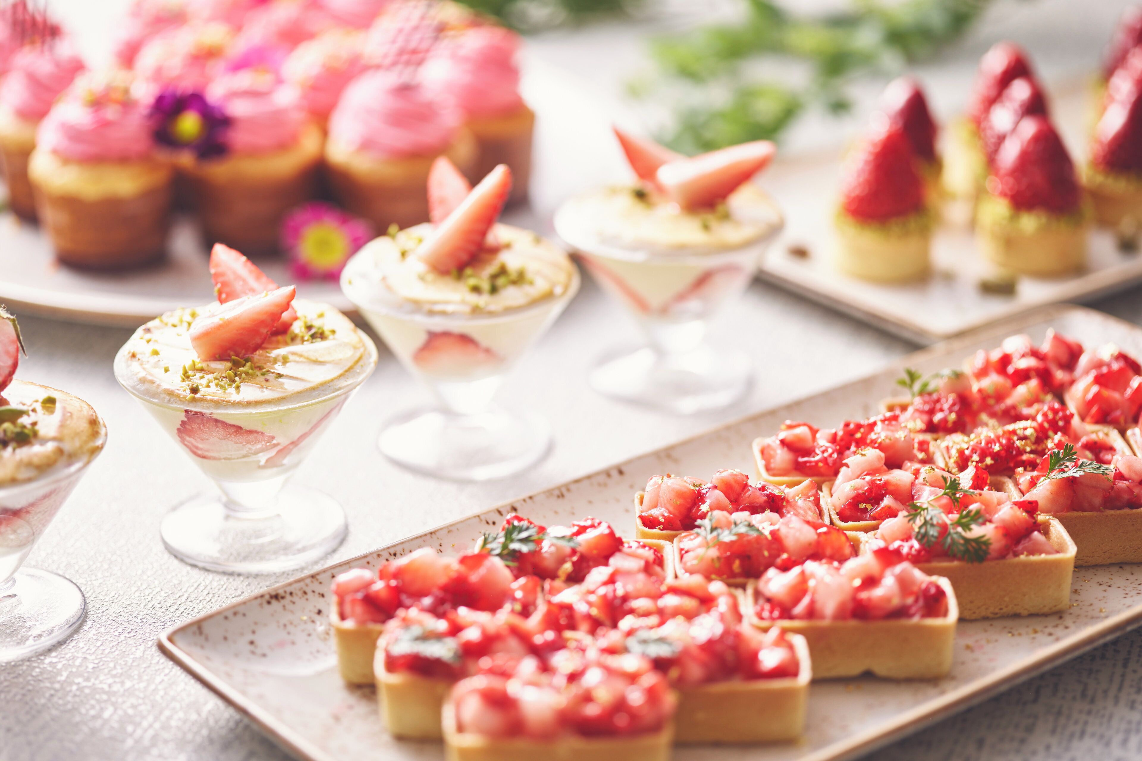 A variety of desserts on a table, including cupcakes, a fruit tart, and a strawberry dish.