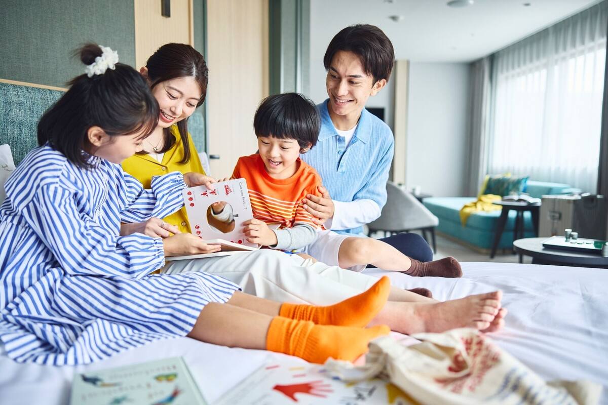 A family of four in a modern hotel room with a bed, a sofa, and a small table.