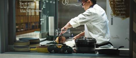 Un chef preparando comida en una cocina con un menú en la pizarra al fondo.