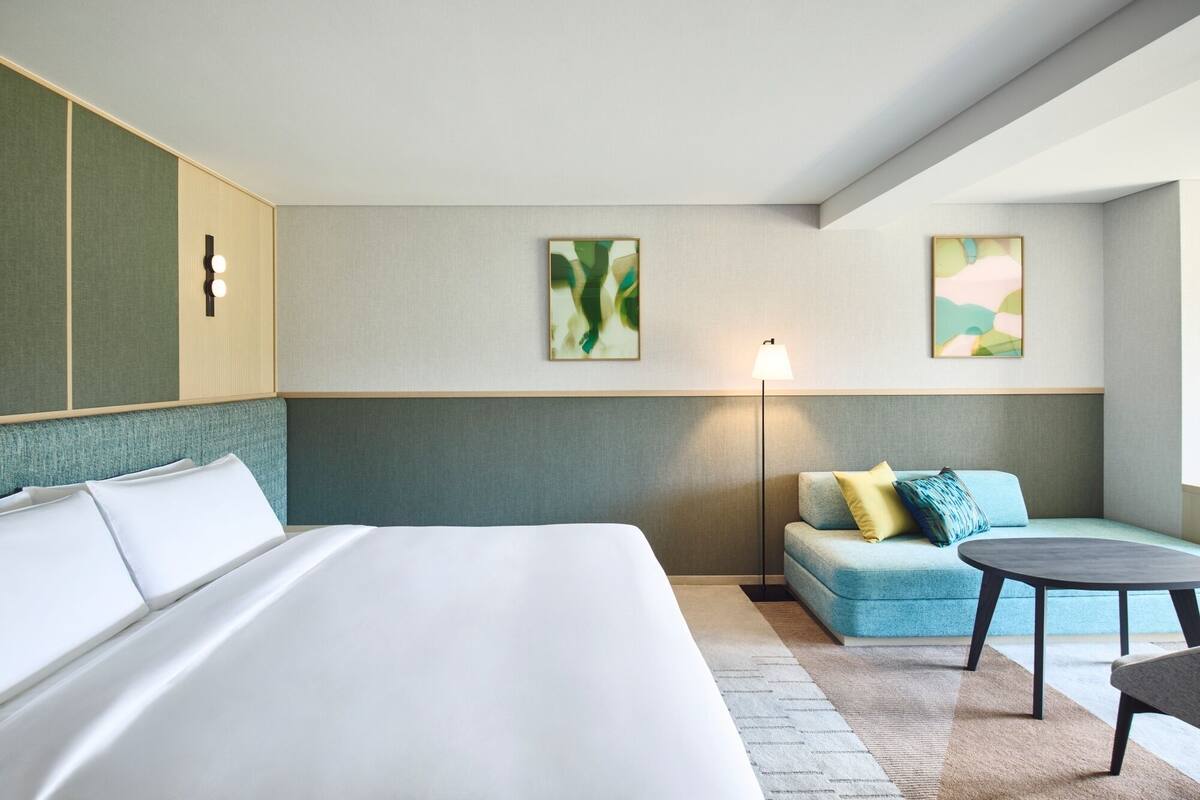 Una habitación de hotel con una cama grande, un sofá, una mesita y dos lámparas de pared.