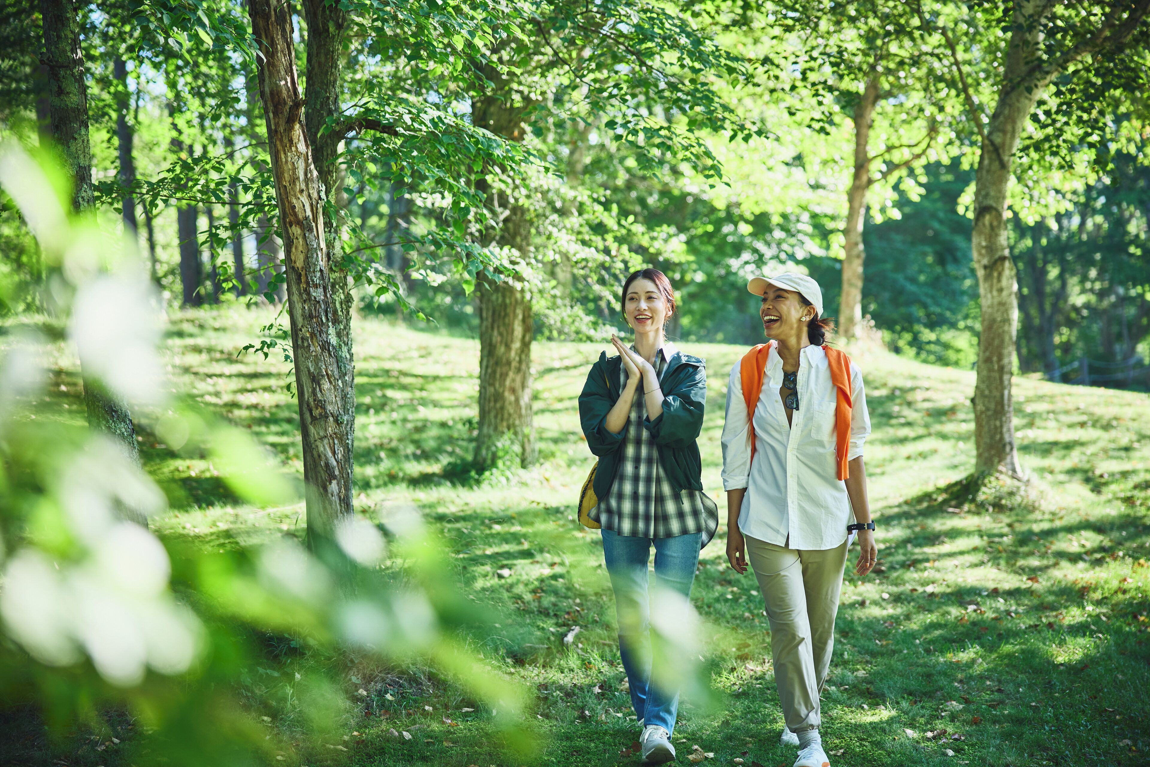 Two people walking in a wooded area with trees and grass.