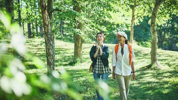 Two people walking in a wooded area with trees and grass.