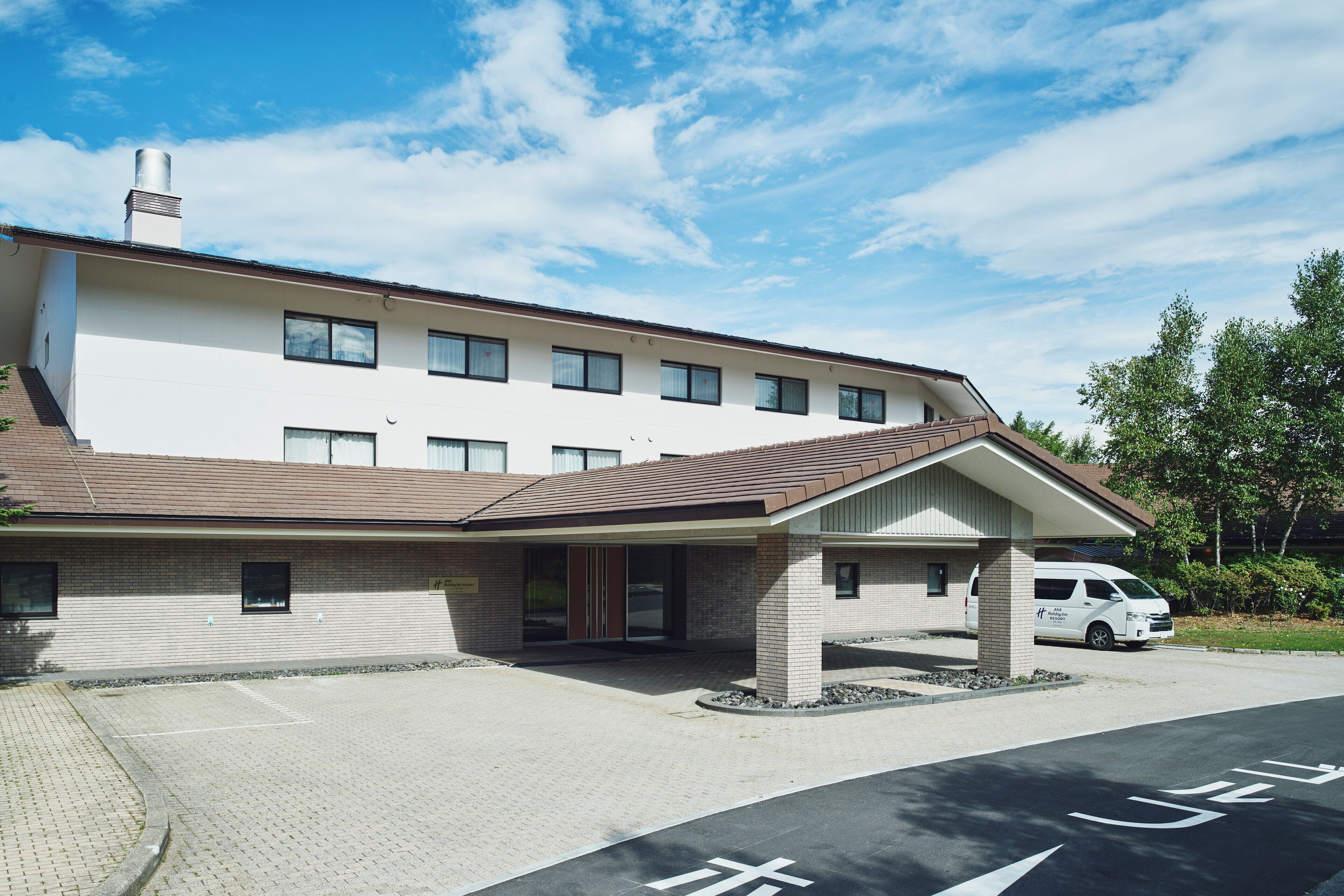 A modern building with a covered entrance, a parking area, and a van parked outside.