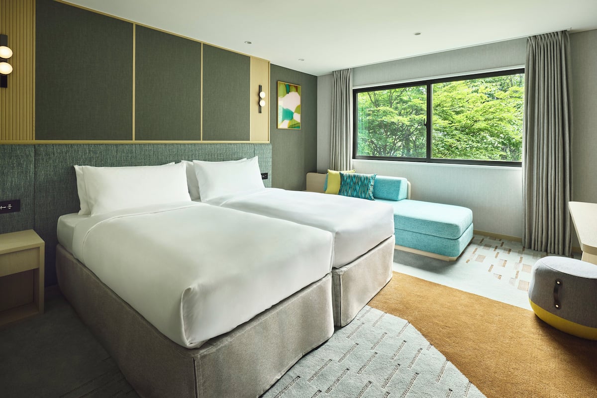 A modern hotel room with a large bed, a sofa, and a window with a view of greenery.