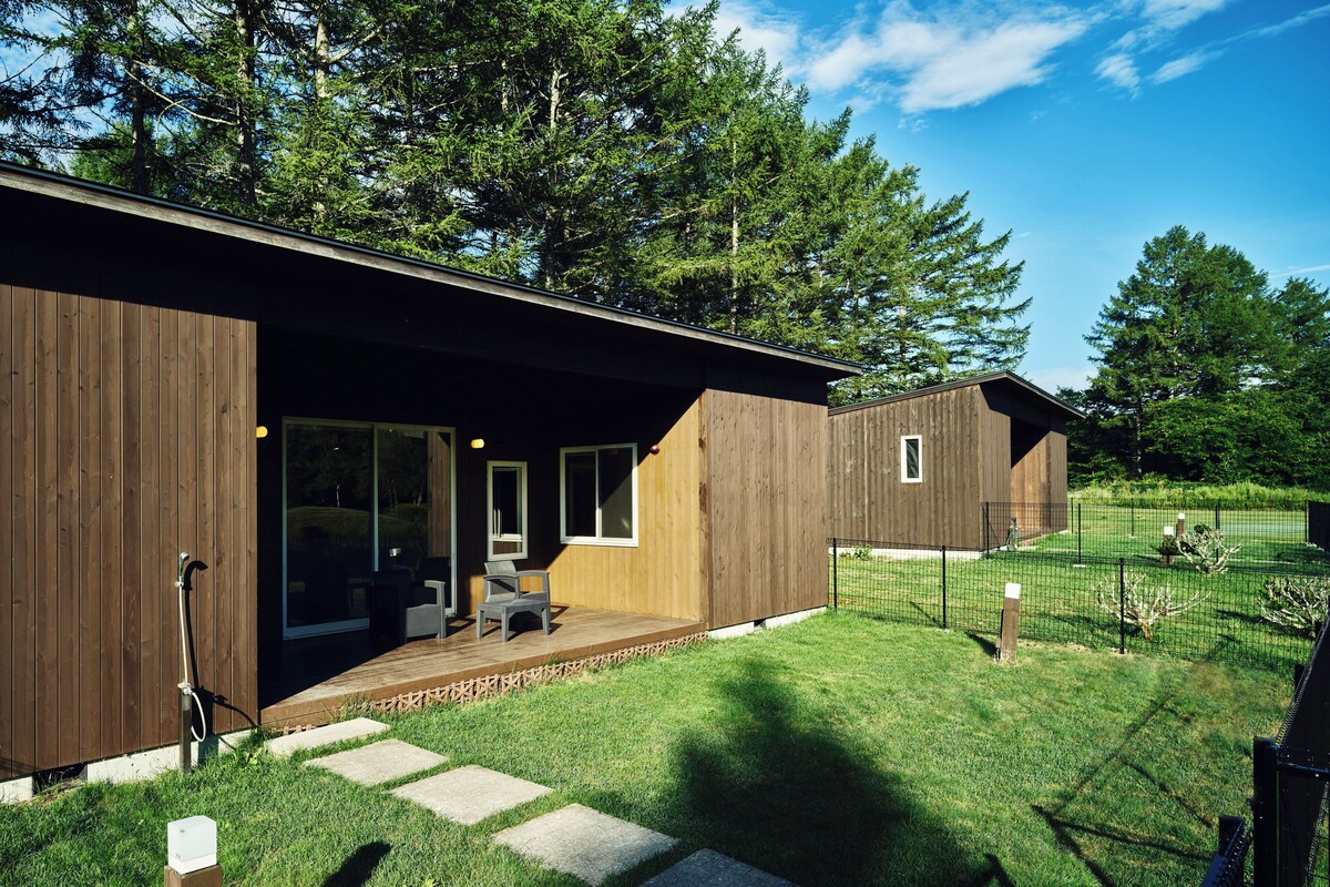 Una casa moderna de madera con un porche cubierto, un patio cercado y una vista despejada del bosque circundante.