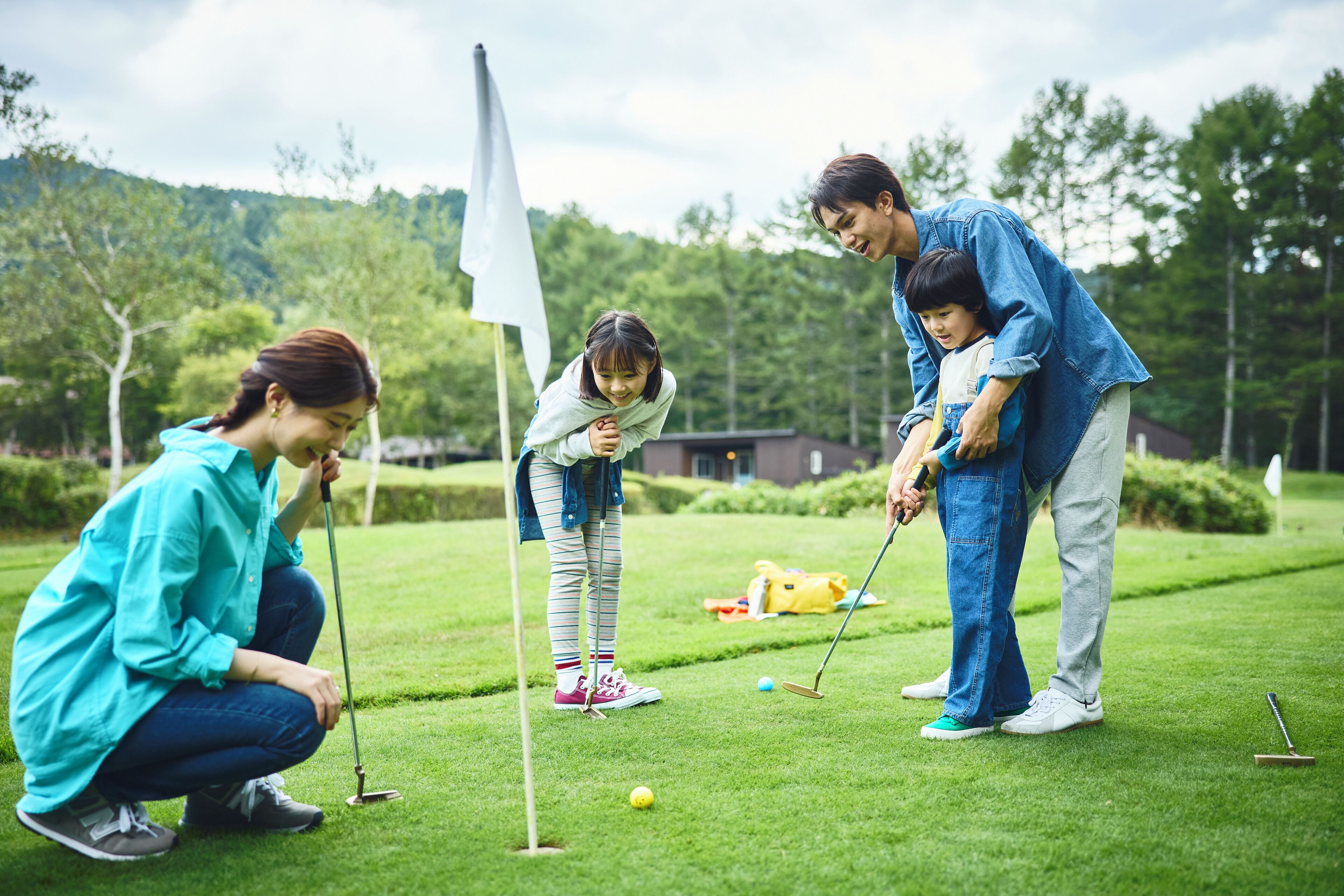A group of people playing golf on a well-maintained course with a flagstick, golf balls, and a putting green.