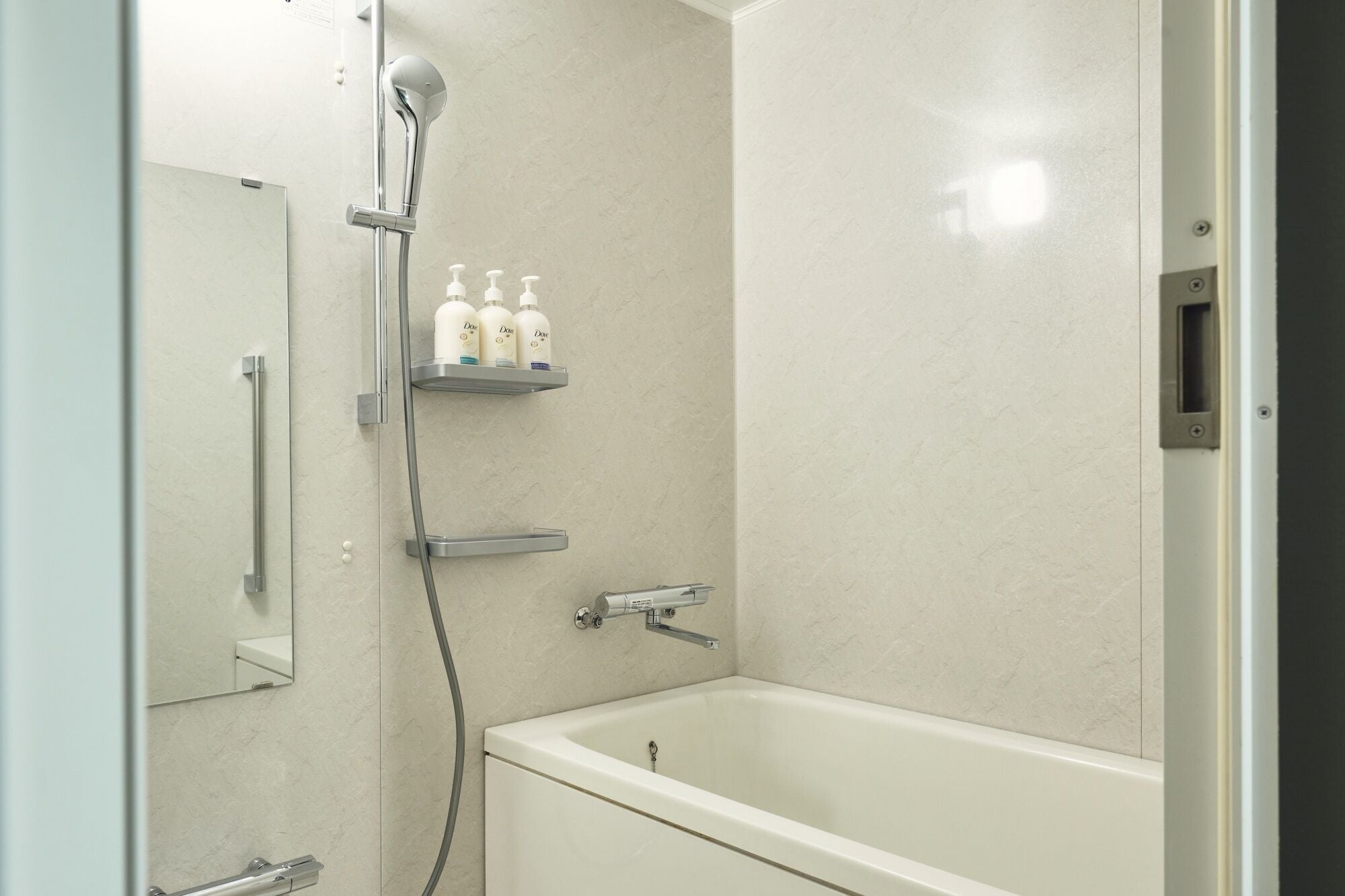 Un baño moderno con bañera, ducha con cabezal de ducha manual y estante con artículos de aseo.