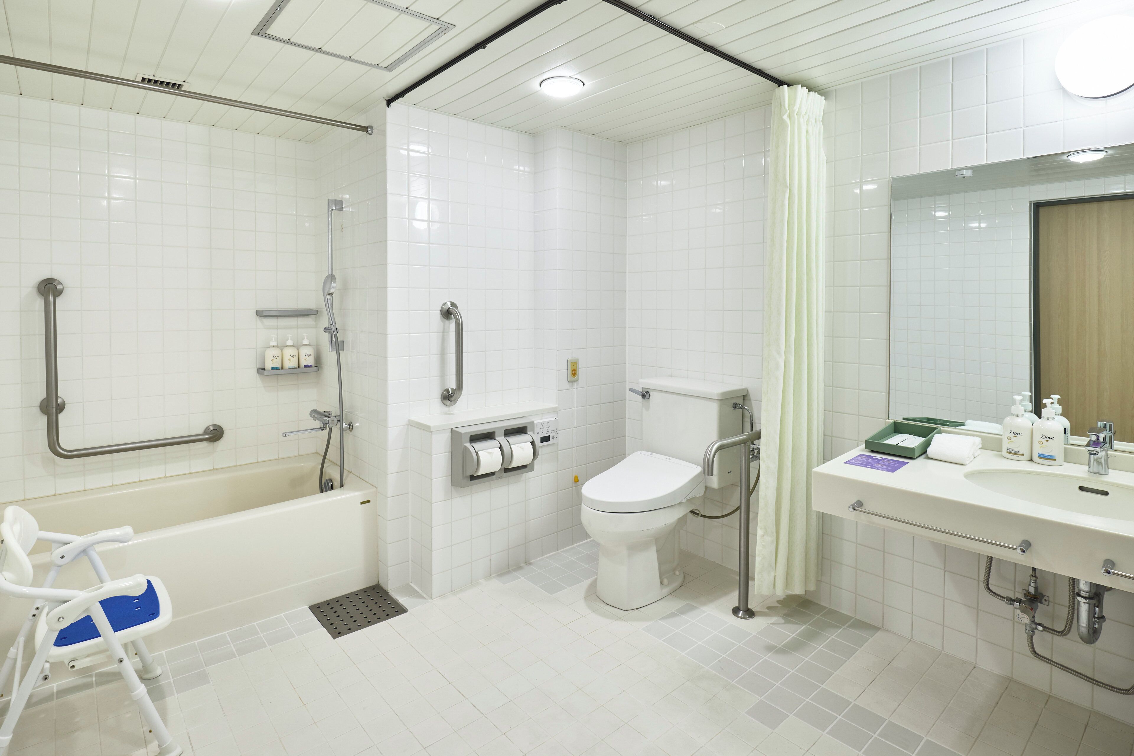 A modern bathroom with a bathtub, toilet, and sink, equipped with grab bars and a shower chair.