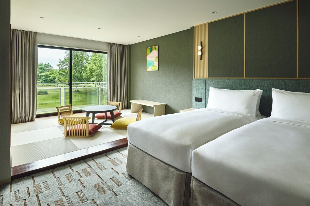 Habitación de hotel con un ventanal grande, una cama, una mesita y una zona de estar con sillas.
