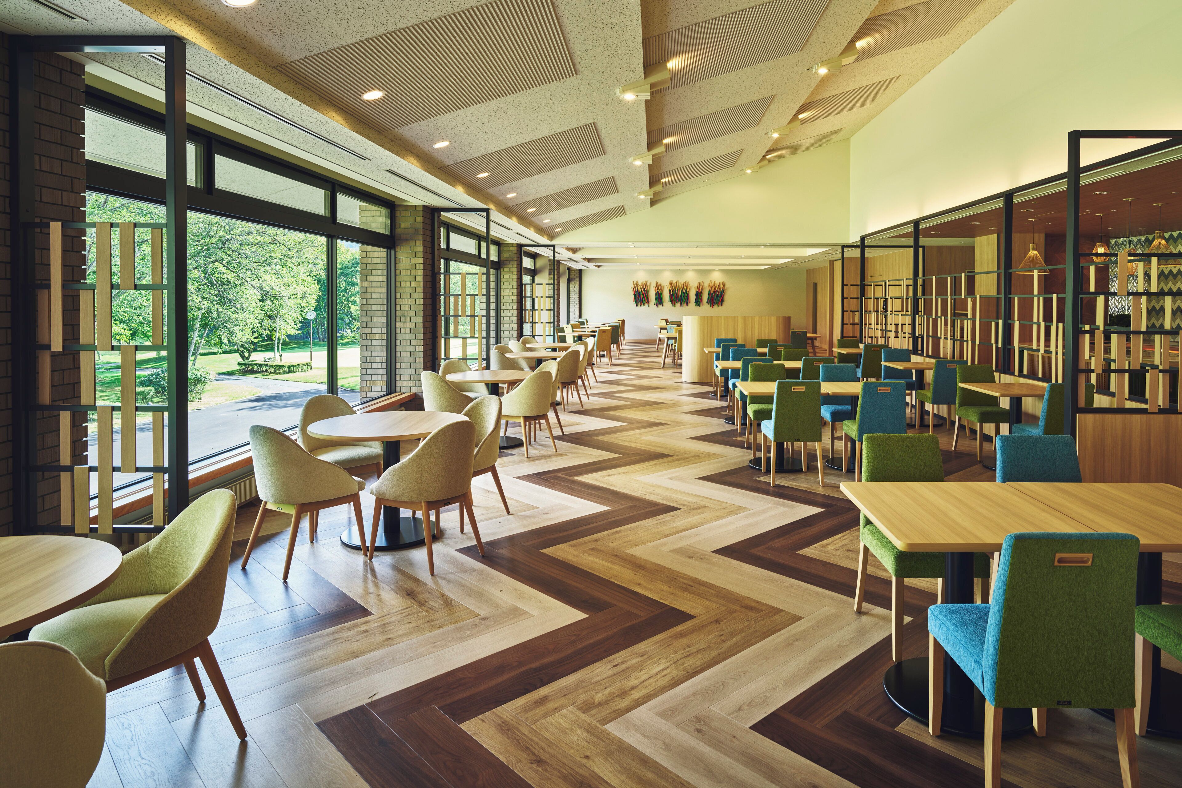 A spacious indoor area with multiple tables and chairs, large windows, and a patterned floor.