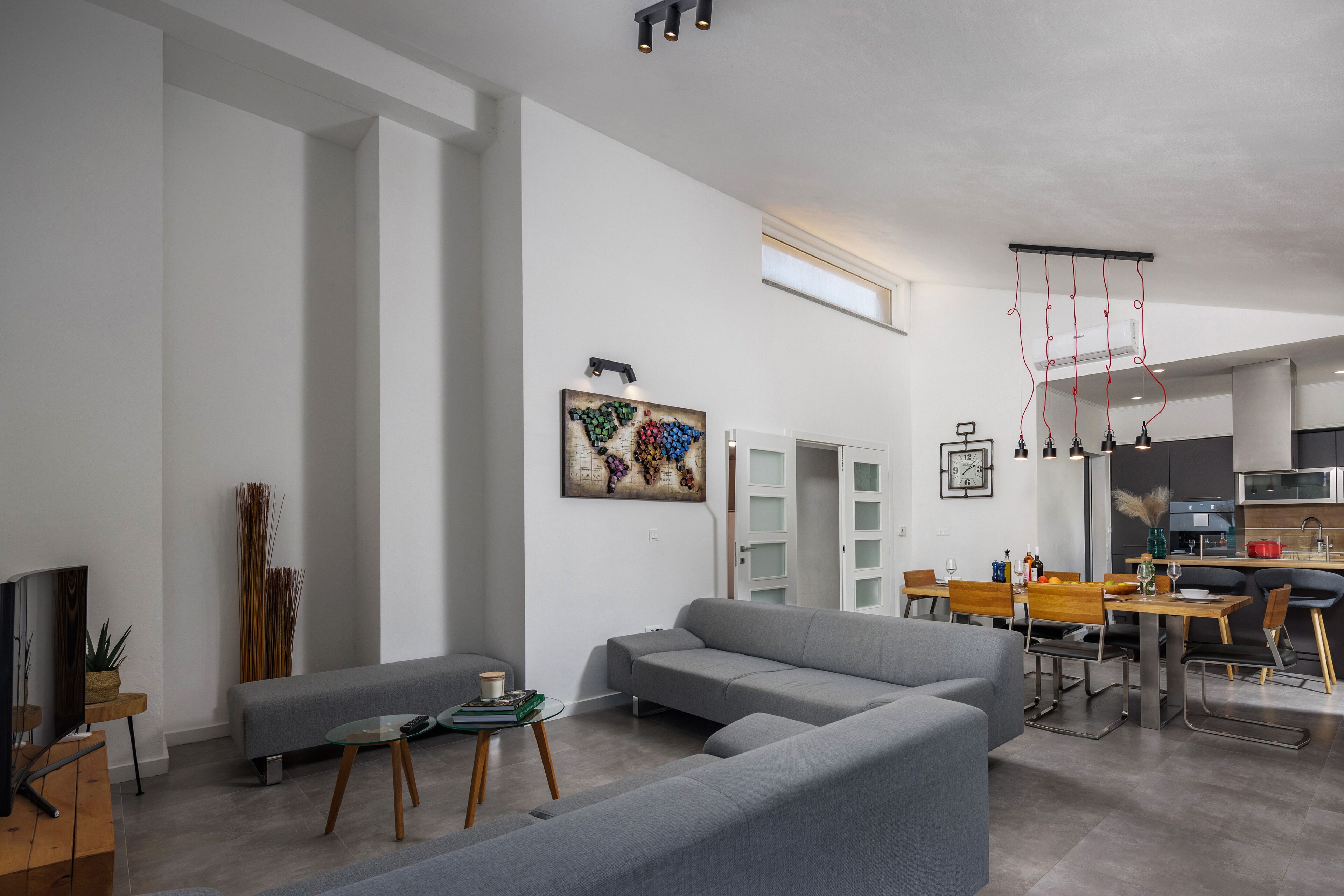 Un salon moderne avec un canapé gris, une table basse en verre et un coin repas comprenant une table et des chaises en bois.