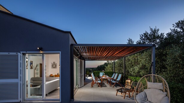 A modern house with a patio area featuring a dining set, chairs, and a hanging chair. - An oasis of tranquility Villa Divinus, with heated pool (Polača)