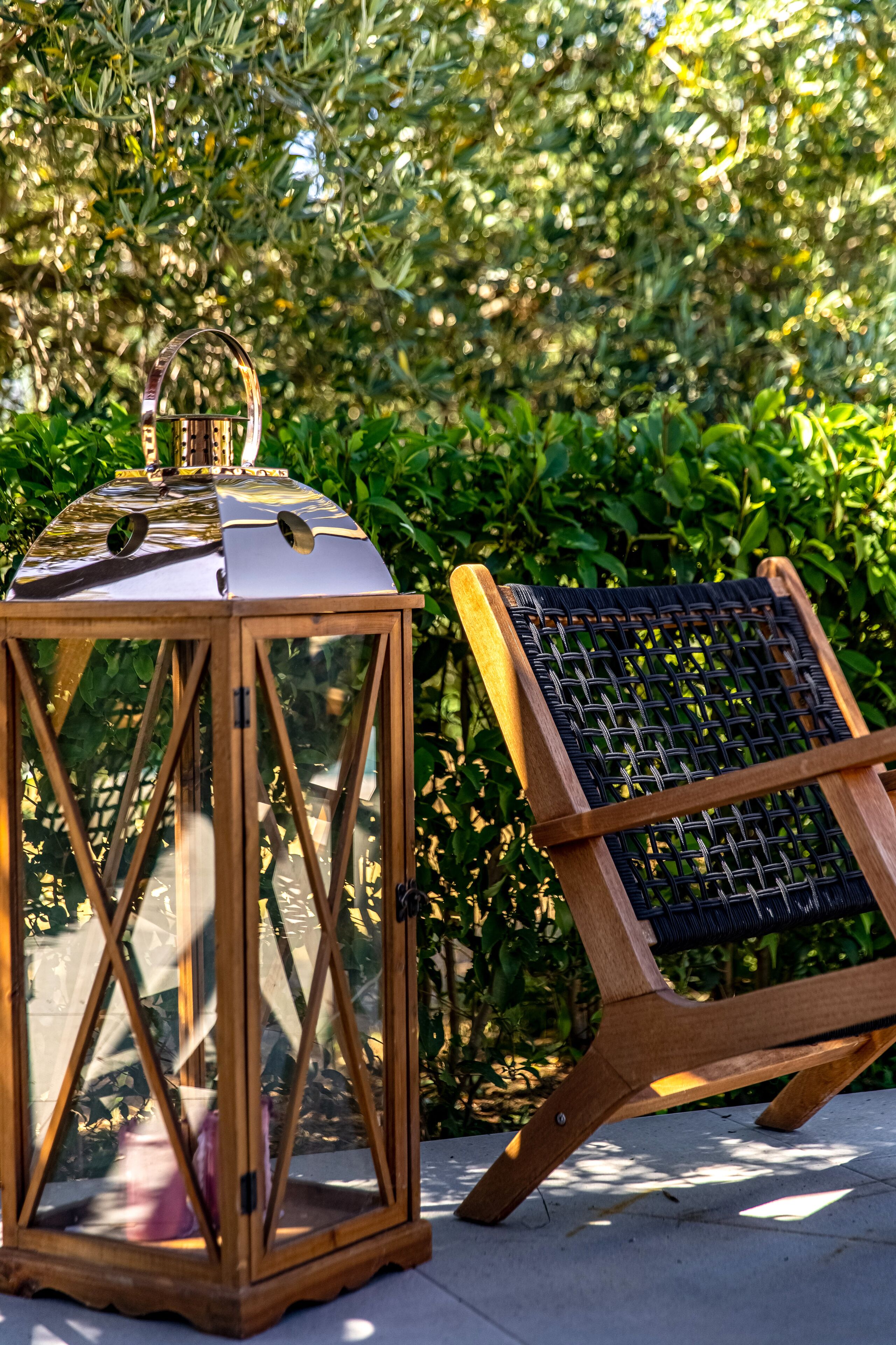 A wooden chair and a glass lantern in a garden setting.