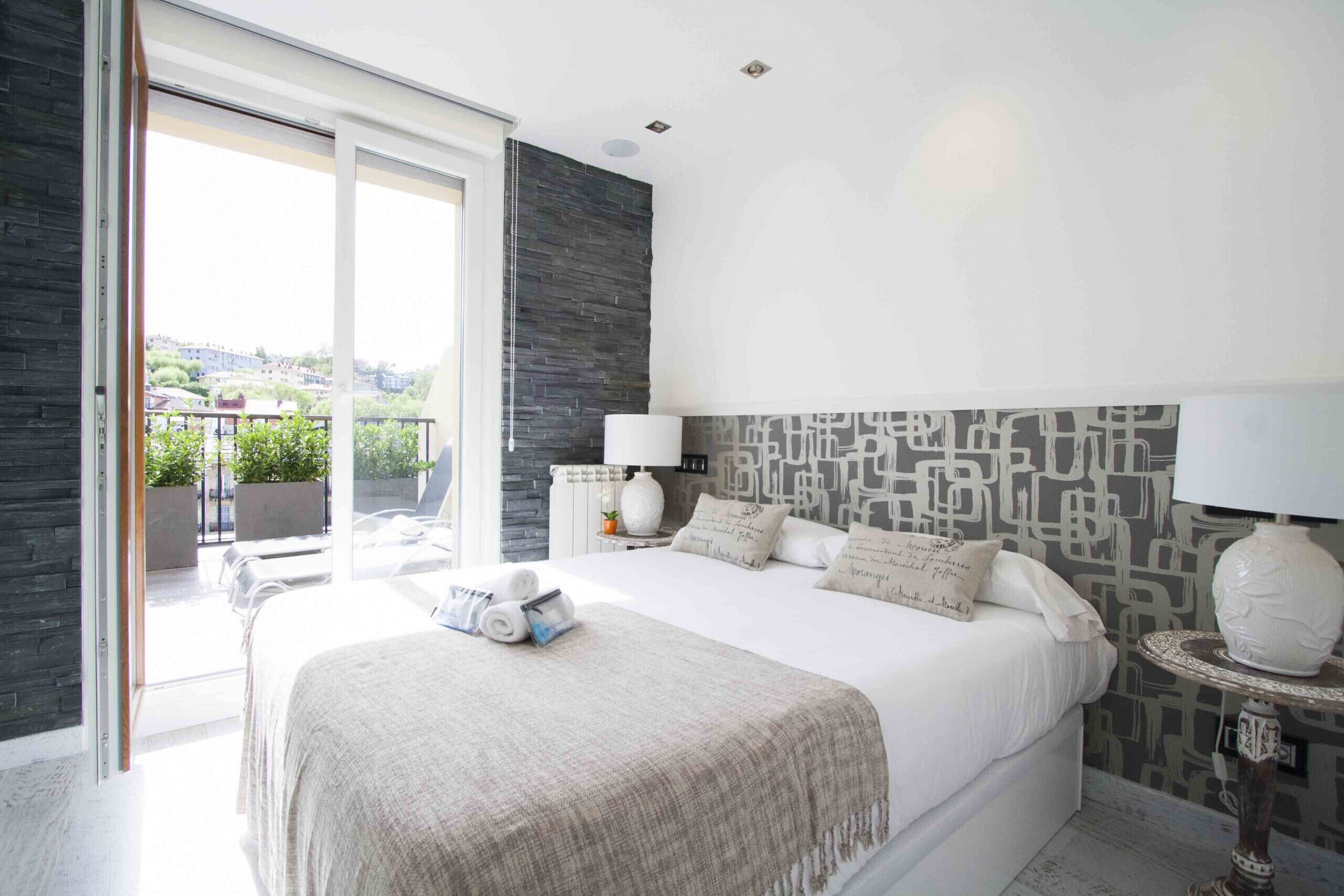 A modern bedroom with a large bed, a view of the outdoors, and a stone accent wall.