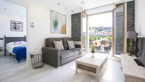 En moderne stue med en grå sofa, et sofabord og udsigt over byen gennem store glasdøre.