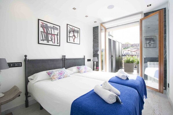 A hotel room with two beds, a balcony with a view, and artwork on the walls. - Da Vinci | The Rentals Collection (San Sebastián)