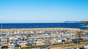 Un port de plaisance où sont amarrés de nombreux bateaux, un ciel bleu dégagé et une route où circulent des véhicules.