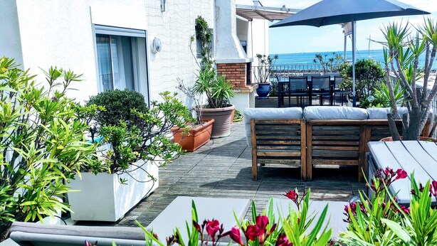 Une terrasse sur le toit avec un banc en bois, des plantes en pot et une vue sur la mer.