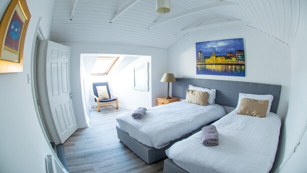 Ein Zimmer mit zwei Betten, einem Nachttisch, einem Stuhl und einem Stadtbild.