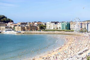 Ein belebter Strand mit Menschen und Sonnenschirmen, ein Riesenrad und Gebäude im Hintergrund.