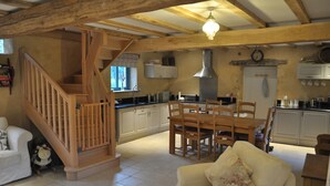Una cocina amplia con vigas de madera, un comedor con mesa y sillas, una escalera y una sala de estar con sofá.