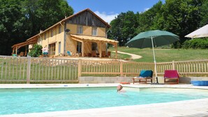 Zona de piscina con una casa al fondo, una valla de madera y mobiliario de exterior.