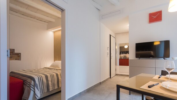 A modern hotel room with a bed, a dining area with a table and chairs, a TV, and a kitchen area in the background. - Vucciria suite behind the cathedral (Palermo)