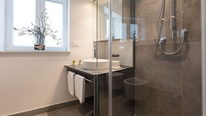 A modern bathroom with a glass-enclosed shower, a white sink, and a window with a vase of flowers. - Vucciria suite behind the cathedral (Palermo)